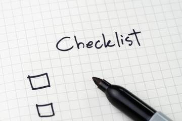 Close-up of notepad with pen and handwriting headline as Checklist with checkbox on table, to do list, prioritize or reminder for project or plan