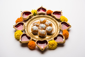 Diwali Rangoli using Diya, flowers and Motichoor Laddu or Boondi Laddoo arranged over white background, selective focus