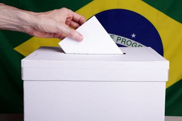 A Brazilian citizen inserting a ballot into a ballot box. Brazil flag in the background