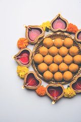 Diwali Rangoli using Diya, flowers and Besan Laddu or Laddoo arrabged over white background, selective focus