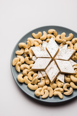 Indian sweet Kaju Katli,/barfi  a diamond shape mithai made using Cashew nuts, milk/khoya and sugar. Served in a grey plate over white background. selective focus