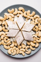 Indian sweet Kaju Katli,/barfi  a diamond shape mithai made using Cashew nuts, milk/khoya and sugar. Served in a grey plate over white background. selective focus