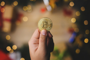 Hand Holding Bitcoin Above Christmas Decoration. Top View © natanaelginting