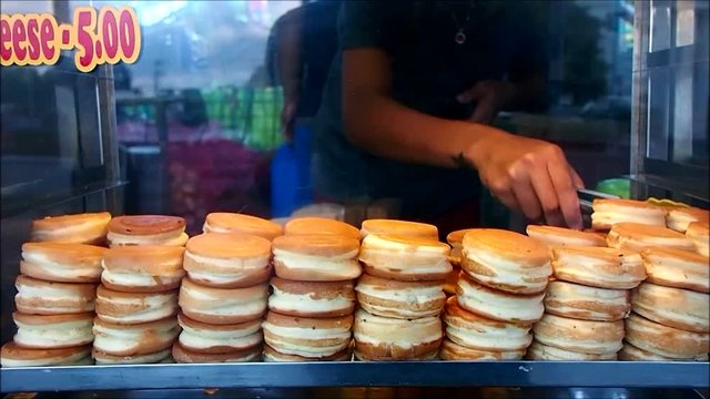 A food vendor stacks mini pancakes on his display shelf of his food cart.