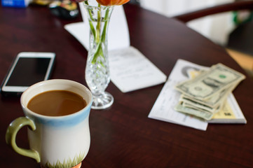 Paying bills and banking concept note book with cup of coffee and dollar bills next to cell phone on desk