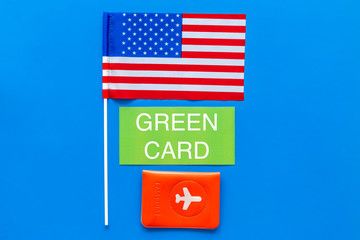 Green card text near passport cover and USA flag top view on blue background copy space. Immigration to United states of america