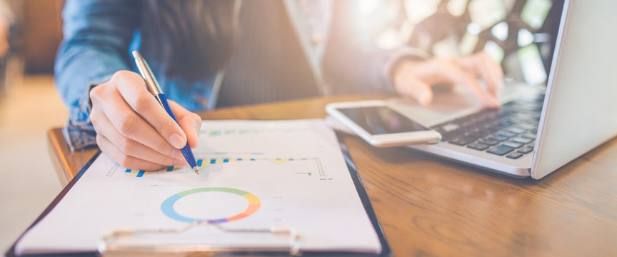 Woman hand writing on charts and graphs that show results with a pen and using a laptop computer working in the office.Web banner.