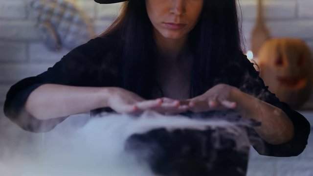 Scary witch making magic potions in her pot with white smoke, Halloween eve