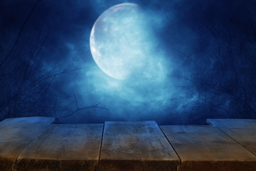 Halloween holiday concept. Empty rustic table in front of scary and misty night sky and full moon background. Ready for product display montage.