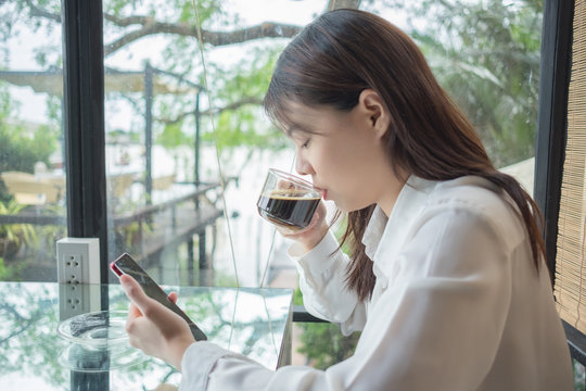 portrait background young business woman drinking coffee and using mobile phone in restaurant with glass are backdrop