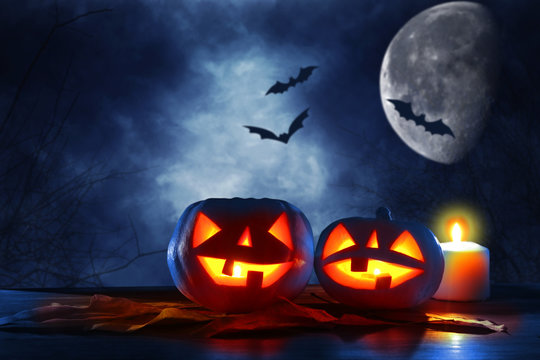 Halloween holiday concept. Pumpkins over wooden table at night scary, haunted and misty forest.
