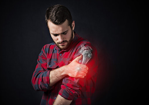 a young man holding onto a sore shoulder against a black background. X-ray