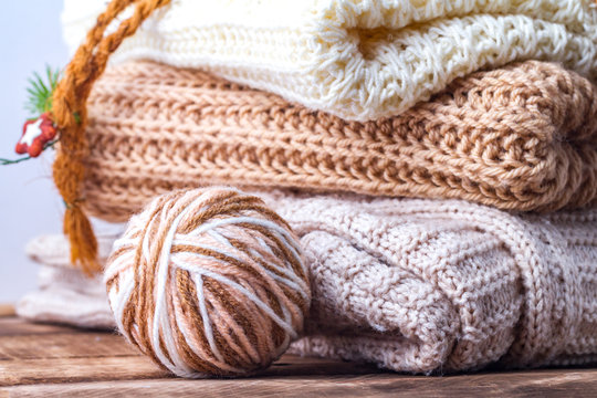 Warm, pastel clothes, knitted, pastel-colored scarves and a ball of knitting yarn on a white background. Winter, autumn clothes.