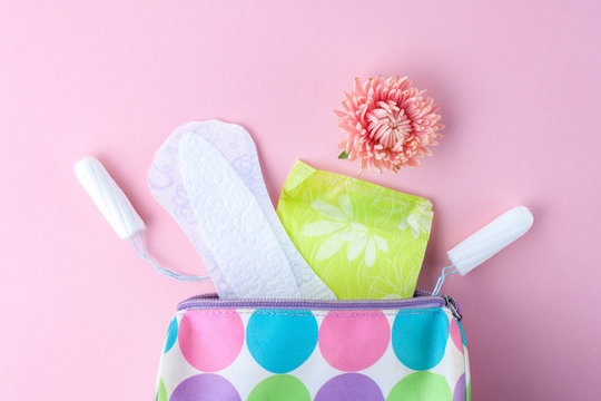 Tampons, feminine sanitary pads, flowers and women's cosmetic bag on a pink background. Hygiene care during critical days. Menstrual cycle. Caring for women's health. Monthly protection