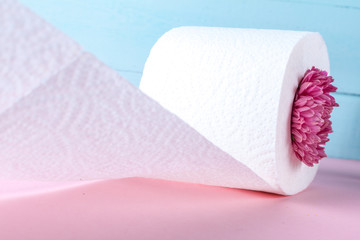 Flavored toilet paper roll and a pink flower on a blue background on a pink table. Toilet paper with a smell. Hygiene concept