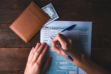 Filling in the U.S. tax form. Tax form 1040, passport, money on a wooden table. Financial concept,...