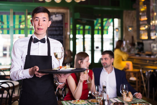 Man waiter is holding tray with wine and salad for clients