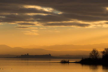 Fototapeta na wymiar Beautiful view of a lTrasimeno lake at sunset, with orange tones, birds on water, Castiglione del Lago town on the background