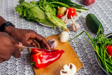 closeup of man hands african american cuts vegetables fry salad pepper, mushrooms, tomato in...