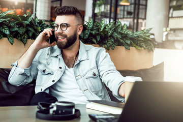 Bearded businessman,blogger sitting in cafe,talking on smart phone,working on laptop, freelancer working in coffee shop.