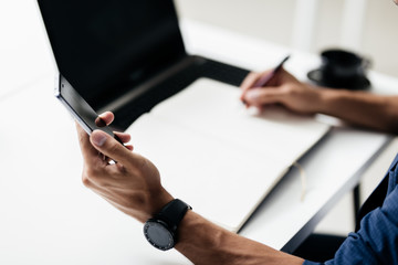 Man makes notes in a notebook on a table and keeps a phone in his hand