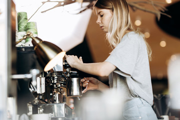A good looking slim blonde with long hair,dressed in casual outfit,is cooking coffee in a modern coffee shop. Process of making coffee is shown.