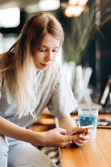 A good looking slim blonde  girl,wearing casual style, sits on the chair and holds a cup of coffee in a cozy coffee shop.