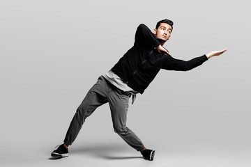 Dark-haired stylish young man wearing a black sweatshirt and gray pants is dancing  street dances