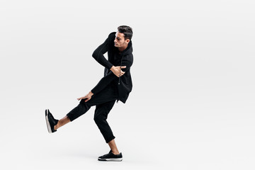 Young dancer dressed in a stylish black clothes lifts one leg up while dancing street dance