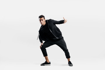 Stylish young man wearing a black sweatshirt and black pants makes stylized movements of  hip-poh