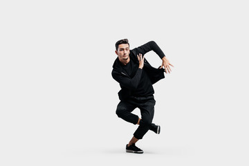 Fototapeta na wymiar Stylish young man wearing a black sweatshirt and black pants makes stylized movements of hip-poh