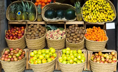 Fototapeten vegetables and fruits in wicker baskets on counter of greengrocery © caftor