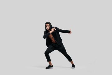 Fototapeta na wymiar Handsome young dancer of street dancing dressed in black pants, a sweatshirt on a naked torso and a hood dances on a white background