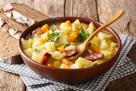 Thick potato soup with sausages and parsley in a bowl with bread close-up. horizontal