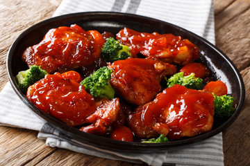 Baked chicken thighs with spicy catalina sauce served with broccoli and tomatoes close-up on a black plate. horizontal