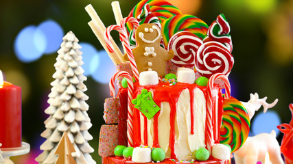 On trend festive candyland Christmas drip cake against festive Christmas tree bokeh lights background.