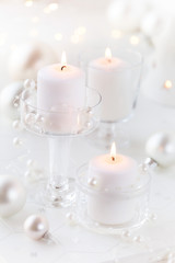 Fototapeta na wymiar Lit white candles in transparent glass candle holders with festive Christmas decorations at the background