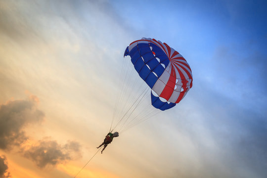 Parasailer Soaring Amidst Sunset Clouds for Thrilling Adventure Tourism