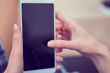 Back view of a woman hands using smart phone with blank screen close up. White phone with a black screen in the hands of a young girl lying on the floor with her feet on the couch