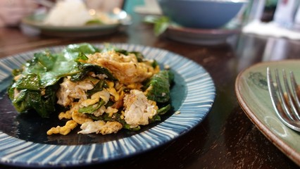 A white plate of delicious Stir-Fried Baegu Leaves or Gnetum gnemon or Melinjo with Eggs on banana leaf. Thai Southern traditional food style with Selective focus.