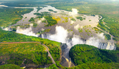 Victoria Falls in Zimbabwe and Zambia, Aerial helicopter photo, green forest around amazing majestic waterfalls of Africa. Livingston Bridge above the river - obrazy, fototapety, plakaty