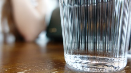 Close up Glass of water on the wooden table with blurry background hand of asian woman in cafe restaurant 