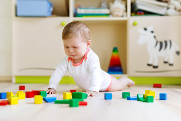 Cute sad crying baby playing with colorful wooden blocks toys