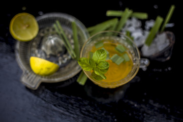 Close up of Iced lemon grass tea in a transparent cup on wooden surface with raw lemon grass green tea in a cup and sugar in a clay bowl with ice cubes in the cup and a piece of ginger and honey.