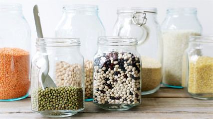 Various cereals, grains and beans in glass jars. Lentils, chickpeas, peas, beans, quinoa, rice and bulgur. Concept  Clean eating. White background and wooden table
