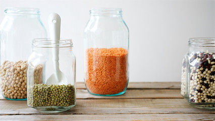 Various beans in glass jars. Beans, mash peas and lentils. White background and wooden table