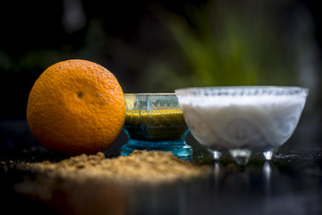Close up of skin whitening method or remedy i.e. raw orange dried skin powder well mixed with yogurt or curd on wooden surface in a transparent glass cup with raw orange.