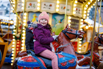 Fototapeta na wymiar Adorable little kid girl riding on a carousel horse at Christmas funfair or market, outdoors.