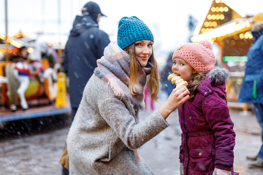 Young mother and daughter eating white chocolate covered fruits on skewer on traditional German Christmas market