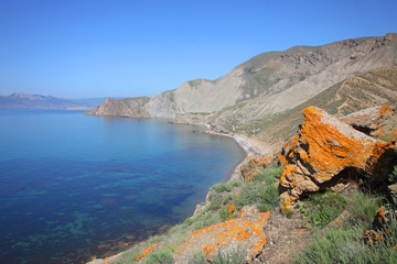 View to the Black blue sea with big orange stone in front in sunny day